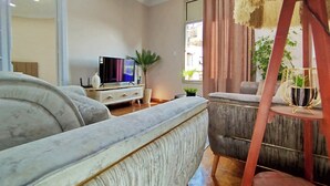 En stue med sofa, fjernsyn, plante og et vindue med gardiner.