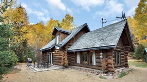 Une cabane en rondins dotée d’un patio, entourée d’arbres aux couleurs automnales.
