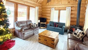 L’intérieur chaleureux d’un chalet en bois, avec une cheminée, des canapés en cuir, un sapin de Noël et une grande table basse en bois.