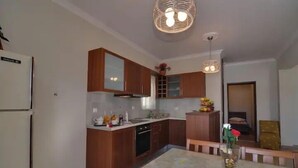 A modern kitchen with wooden cabinets, a built-in oven, and a dining area with a table and chairs. - Memories of Milos (Milos)