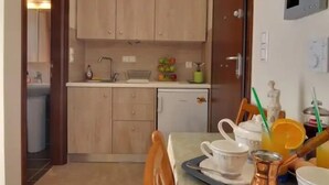 A compact kitchen with wooden cabinets, a dining table set with dishes, and a small refrigerator. - Memories of Milos (Milos)