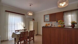 A compact kitchen with wooden cabinets, a refrigerator, and a dining area with a table and chairs. - Memories of Milos (Milos)