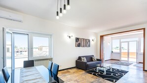 Moderni olohuone, jossa on ruokailutila, suuret ikkunat ja näkymä kaupunkiin.