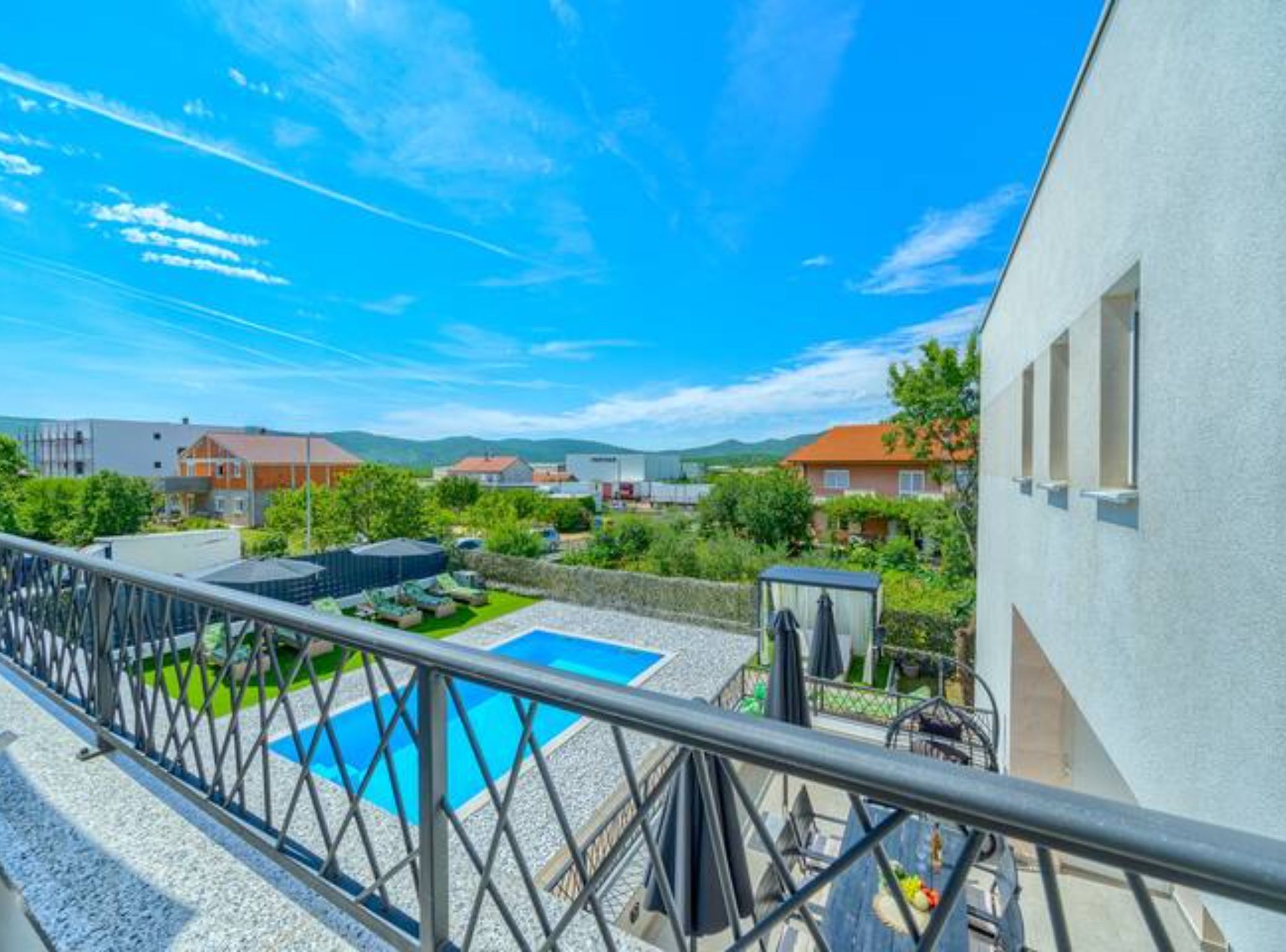 Un quartier résidentiel doté d’une piscine, d’un balcon grillagé et offrant une vue sur les maisons et les collines environnantes.