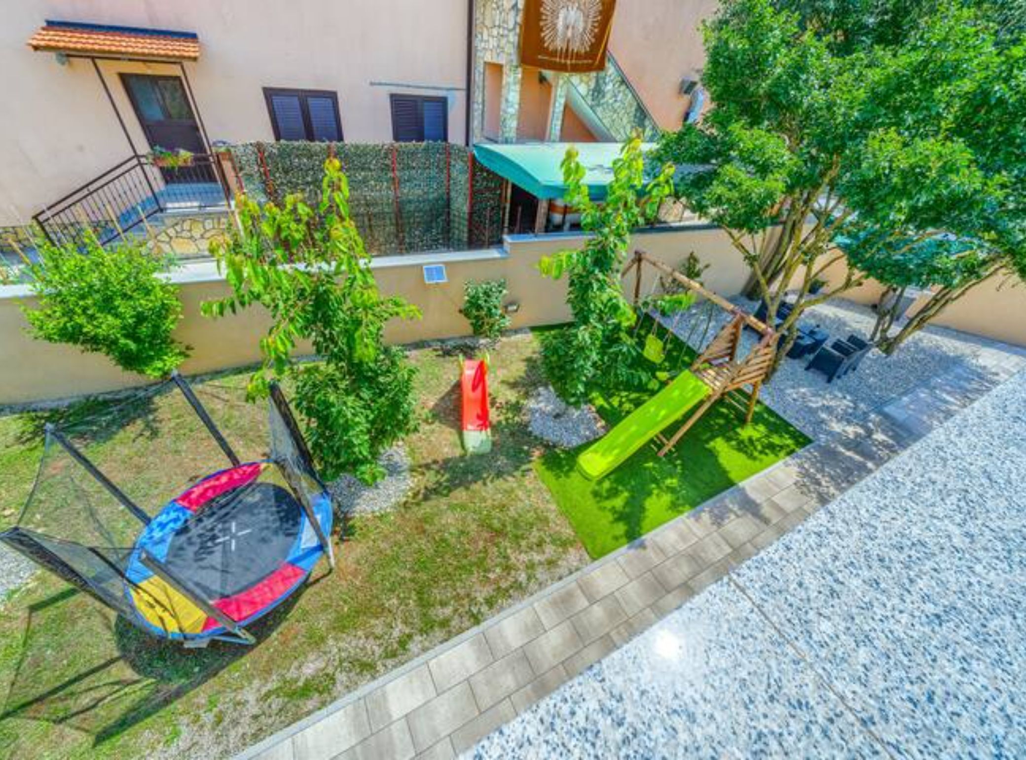 A rooftop garden with a trampoline, a swing set, and a small tree.