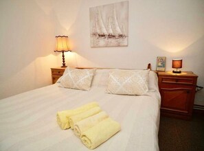 A neatly made bed with two pillows, a bedside lamp, and a painting of sailboats on the wall. - Apartment Nonna (Seget)