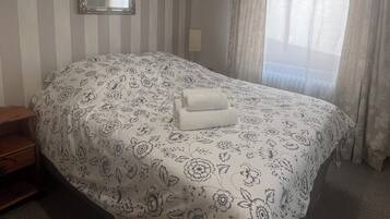 A hotel room with a bed, a bedside table, a mirror, and a window with curtains.