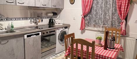 Une cuisine de taille réduite avec un coin repas, comprenant une nappe à carreaux, des chaises en bois et un sol carrelé.