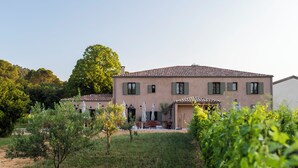 A two-story building with a tiled roof, green shutters, and a patio area with outdoor furniture.