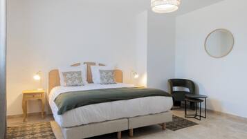 Een keurig opgemaakt slaapkamer met een bed, bedlampjes, een stoel en een klein tafeltje.