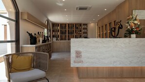 A reception area with a marble counter, wooden shelving with bottles, a wicker chair, and a large window.