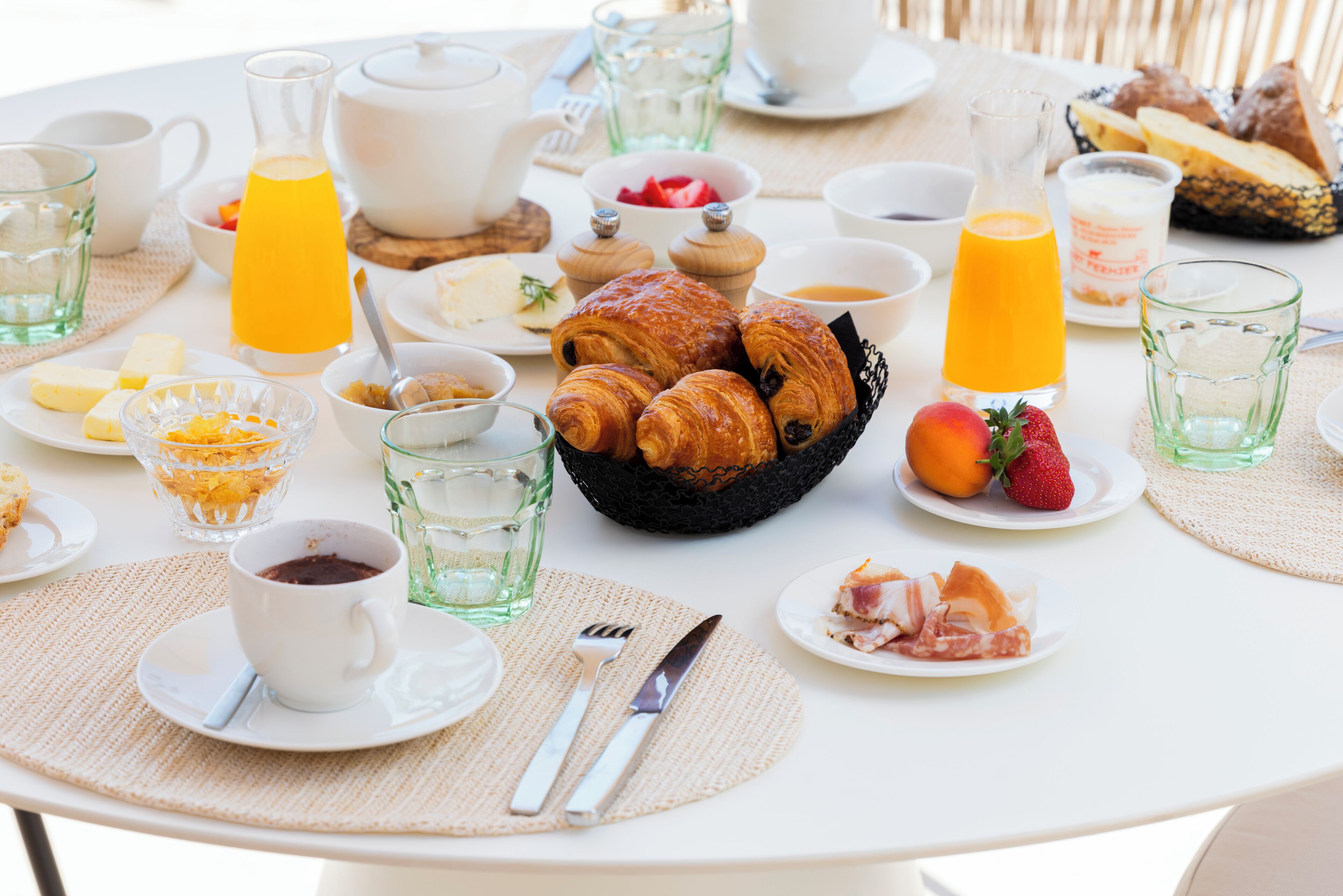 A breakfast table with croissants, fruit, coffee, and juice.
