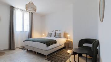 Quarto com uma cama, luminárias de cabeceira, uma cadeira e uma pequena mesa.