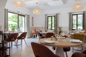 Un comedor con mesas redondas, sillas marrones e iluminación colgante.
