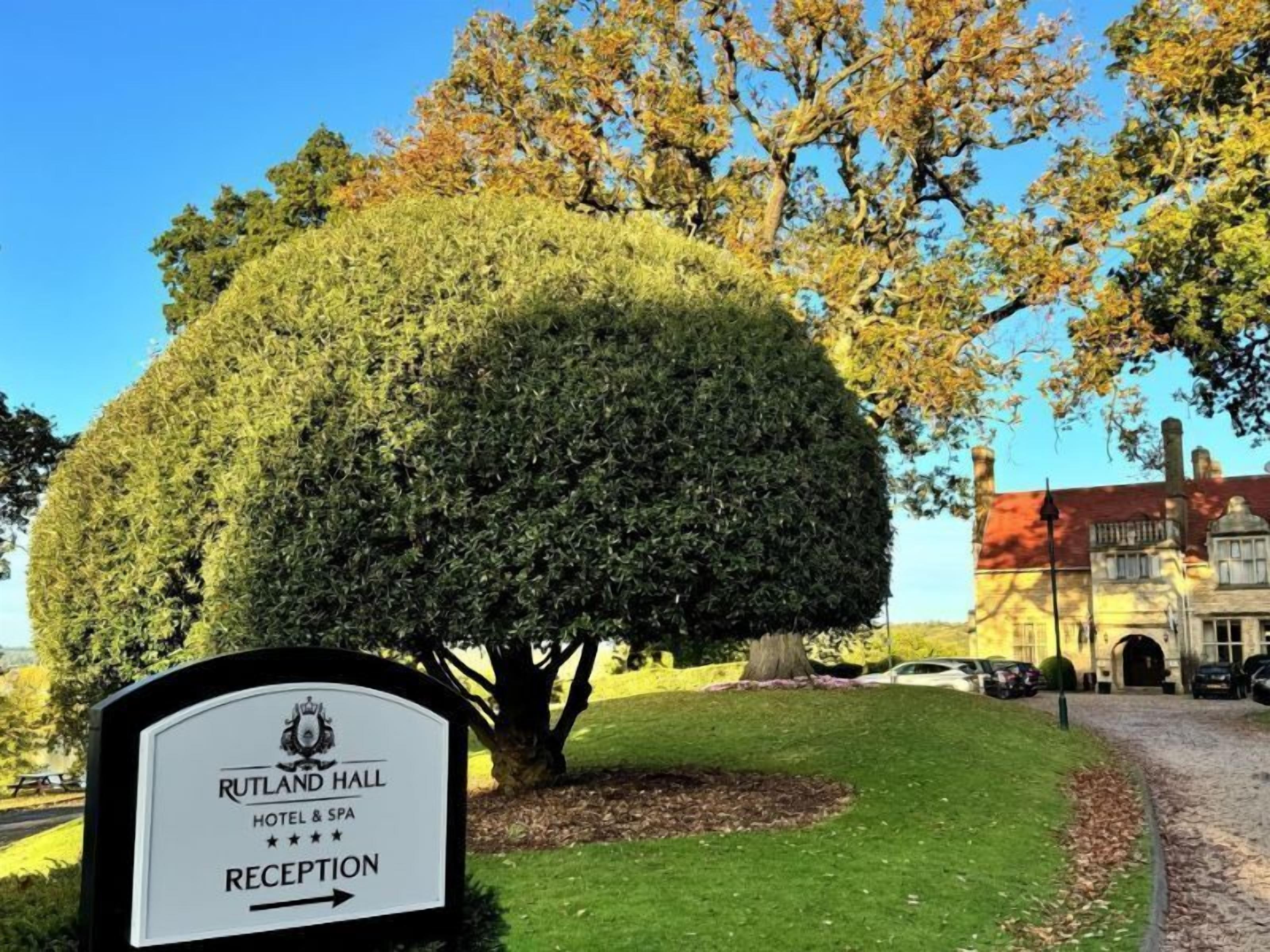 A reception sign for Rutland Hall Hotel & Spa with a well-manicured lawn and a large tree in the background.