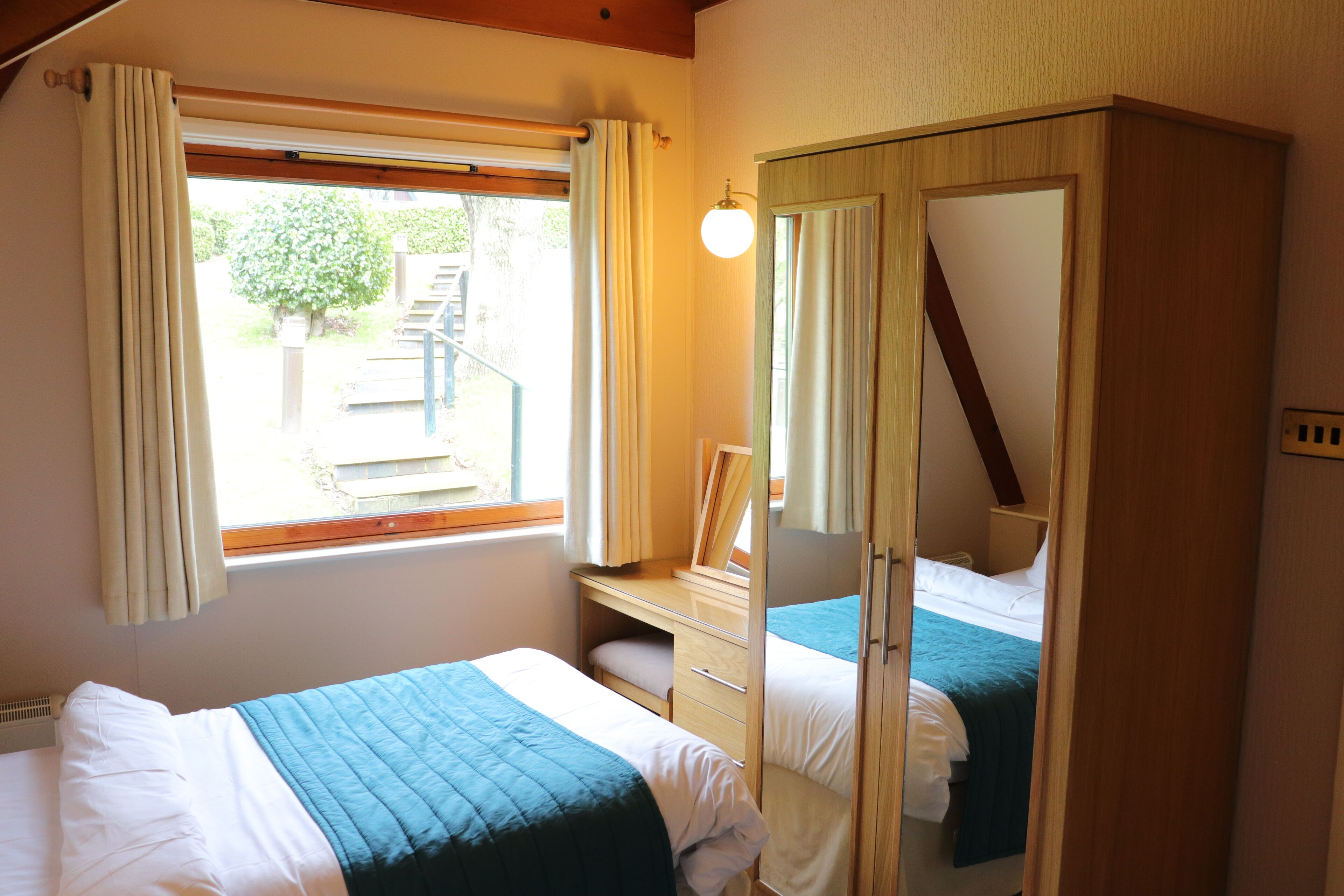 A bedroom with two beds, a wardrobe, a desk, and a window with curtains.