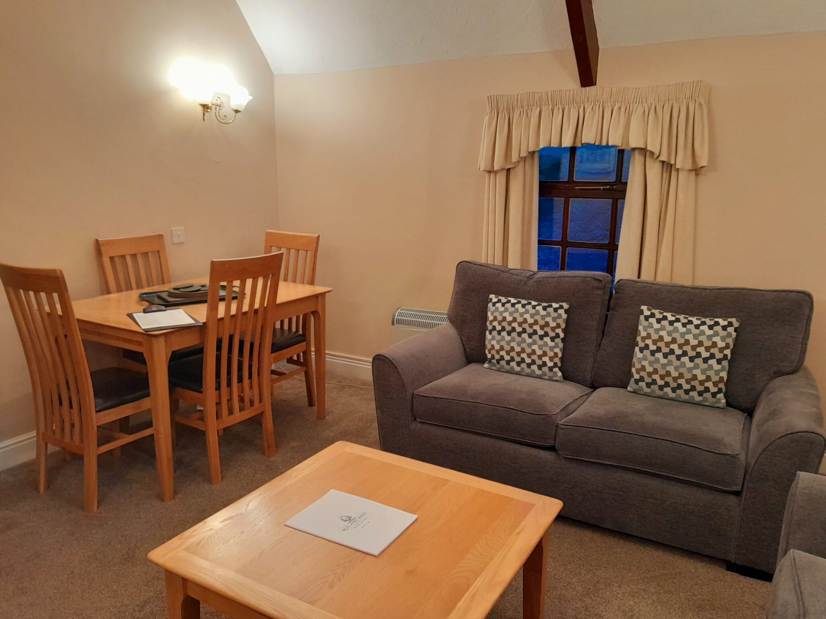 A cozy living room with a brown sofa, two patterned pillows, a wooden coffee table, and a dining table with chairs.