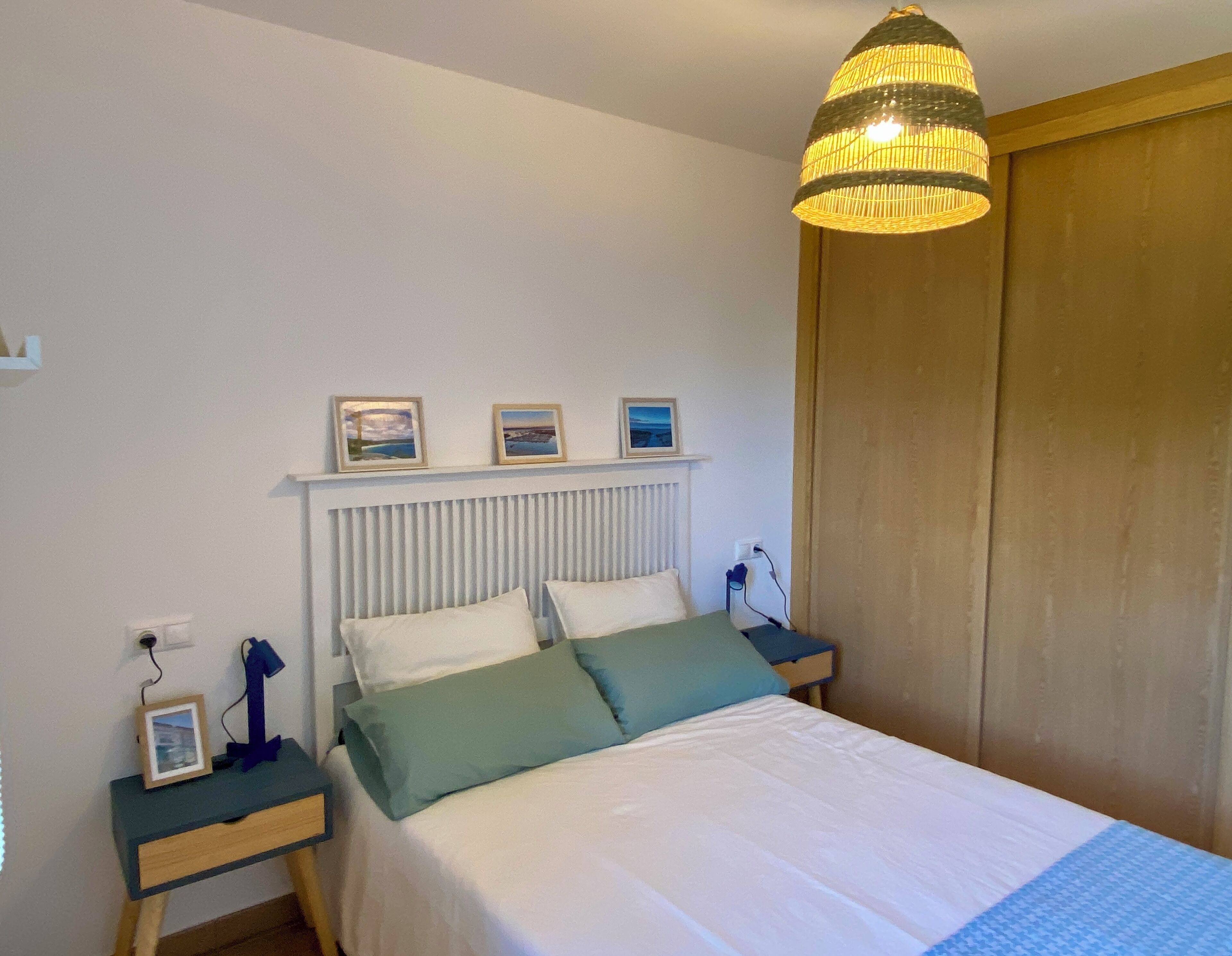 Ein Schlafzimmer mit einem Bett, Nachttischen, einer Hängeleuchte und einem Holzschrank.