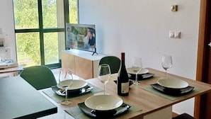A dining area with a wooden table set for four, a television on a cabinet, and a window with a view of trees. - Apto Las Dunas de Langosteira en Finisterre (finisterre)