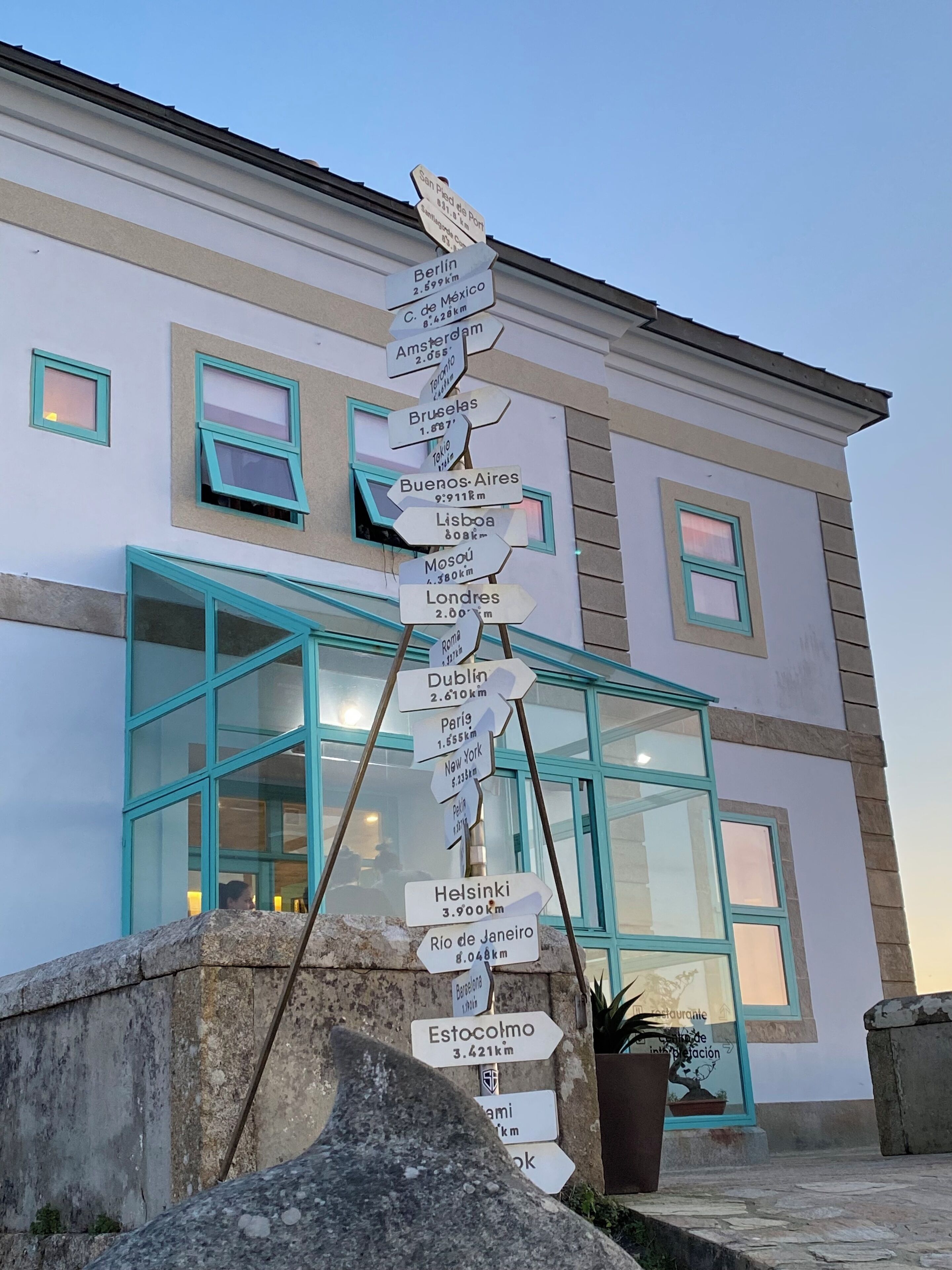 A signpost with directional arrows pointing to various cities and their distances in kilometers.