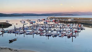 A marina with numerous boats docked, a sandy beach, and a clear sky with a visible moon. - Apto Las Dunas de Langosteira en Finisterre (finisterre)