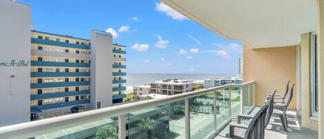 A balcony with a glass railing overlooking a cityscape and the sea.