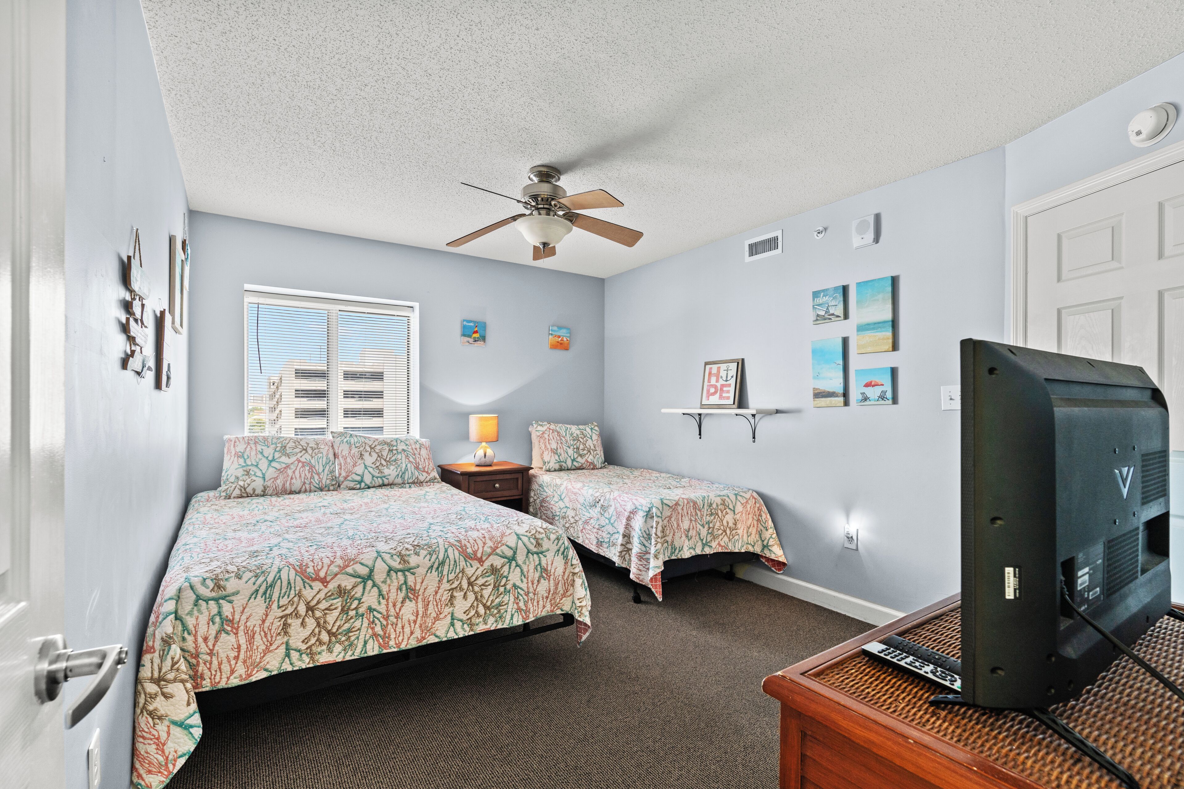 A bedroom with two beds, a ceiling fan, a TV, and artwork on the walls.