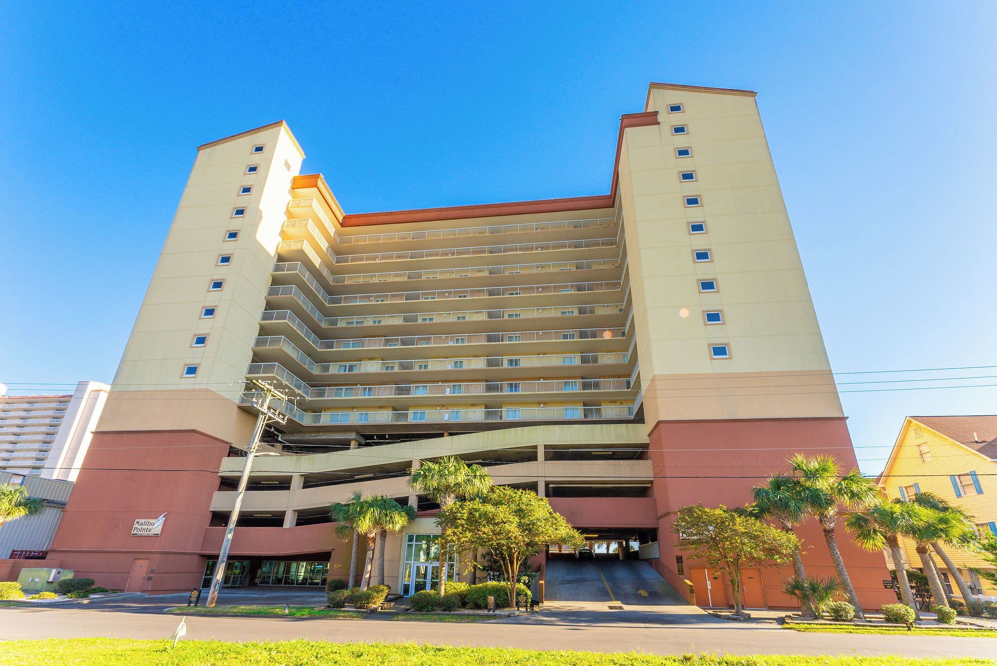 Un hotel de varios pisos con una entrada principal, un garaje para estacionar y un cielo azul despejado.
