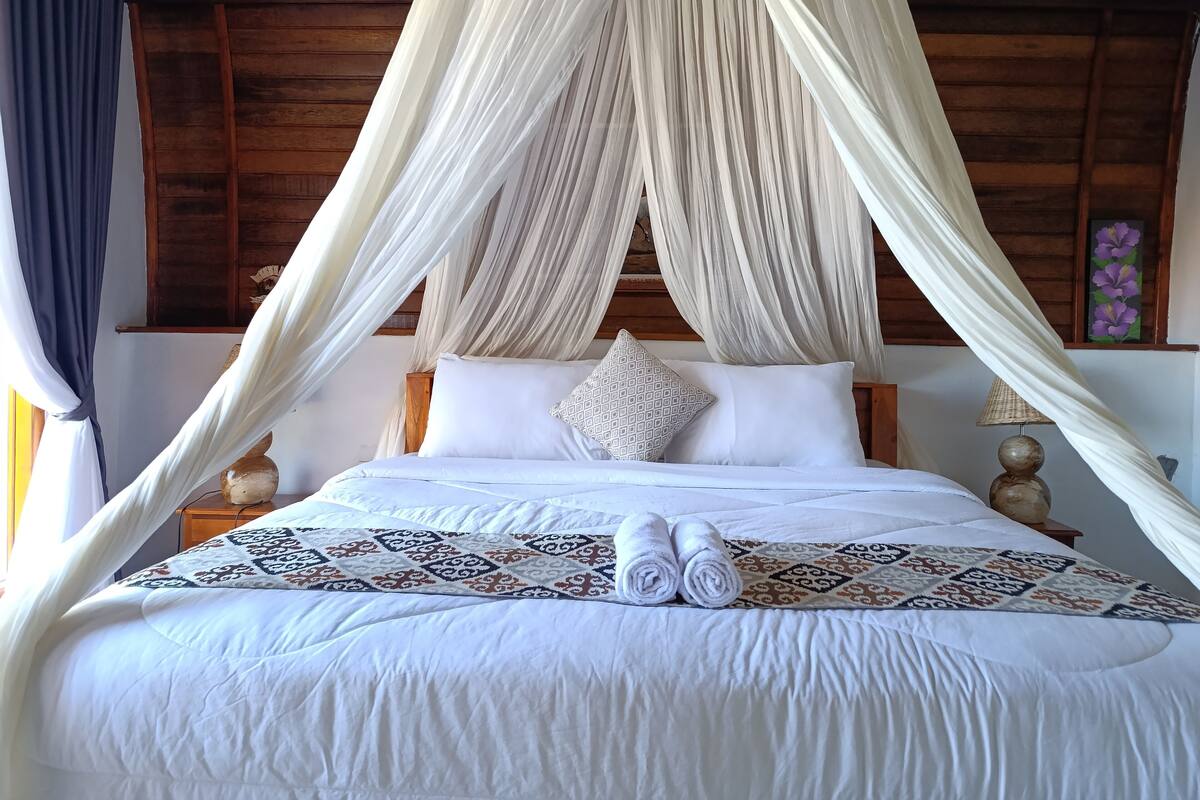 A bed with a canopy, pillows, and rolled towels.