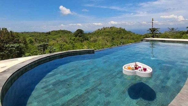 A clear blue infinity pool with a floating bar, surrounded by lush greenery and a clear sky. - Kubuhill Sunset Bungalow (Penida Island)