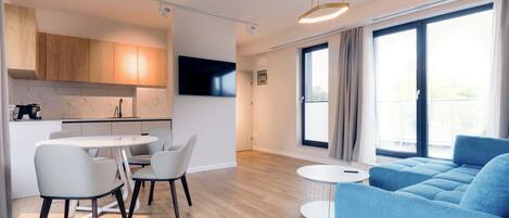 Una sala de estar moderna con un sofá azul, una mesa de comedor con sillas, y una zona de cocina con armarios de madera y un televisor.