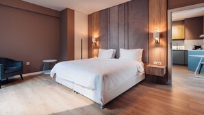 Une chambre d’hôtel moderne avec un grand lit, des tables de chevet, une chaise et une vue sur la cuisine.