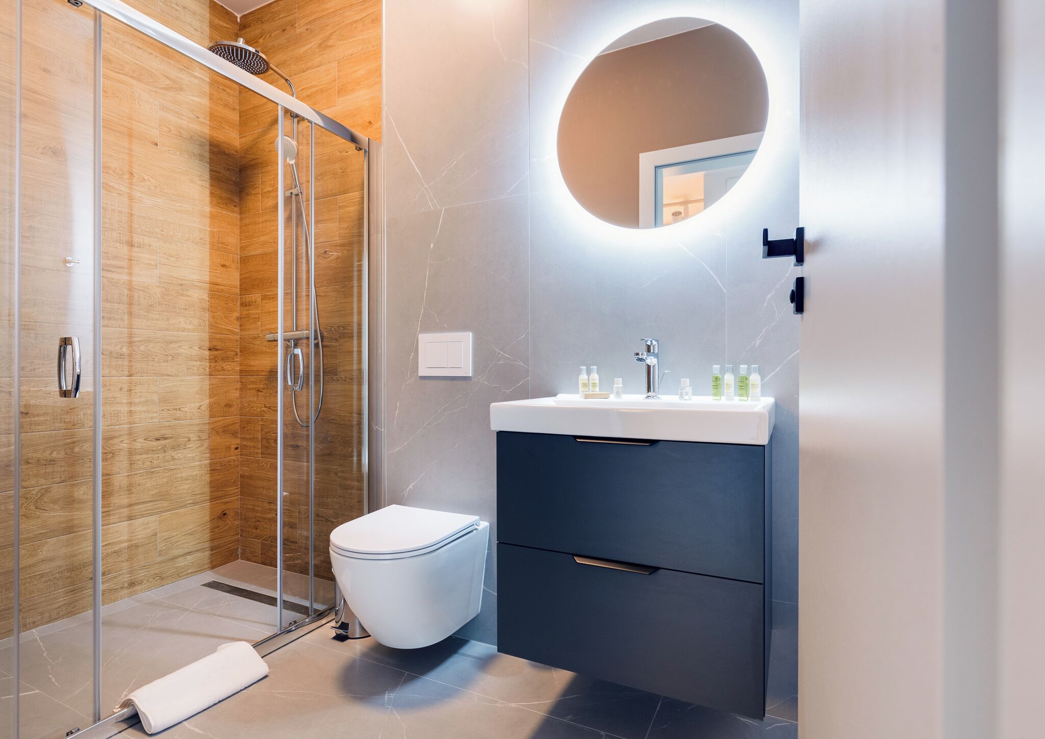 A modern bathroom with a glass shower enclosure, a white toilet, a dark vanity with a mirror, and a sink with toiletries.