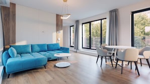 Un salon moderne avec un canapé d’angle bleu, une table basse ronde et un coin repas avec des chaises.