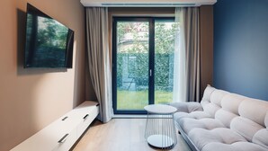 Un salon moderne comprenant un canapé, un téléviseur fixé au mur, une porte-fenêtre coulissante donnant sur un jardin et une petite table ronde.
