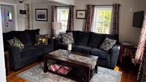 A cozy living room with two dark sofas, a wooden coffee table, and patterned cushions. - Bellecroft House - Beautifully renovated, stunning water-front getaway property (Trinity East)