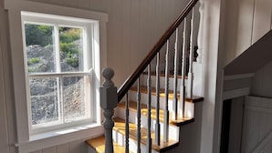 A staircase with wooden steps and white balusters, leading to a landing with a white door. - Bellecroft House - Beautifully renovated, stunning water-front getaway property (Trinity East)