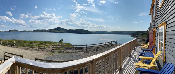 Terraza de madera con sillas que da a un lago y colinas distantes.