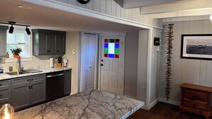 A modern kitchen with dark cabinets, a marble countertop, and a wall-mounted clock. - Bellecroft House - Beautifully renovated, stunning water-front getaway property (Trinity East)