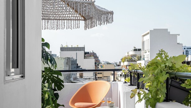 A narrow outdoor corridor with patterned flooring, a small orange chair, and a potted plant. - Mate Levinski - By HOMY (Tel Aviv)