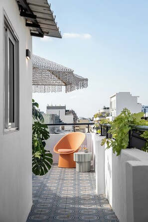 A narrow outdoor corridor with patterned flooring, a small orange chair, and a potted plant. - Mate Levinski - By HOMY (Tel Aviv)