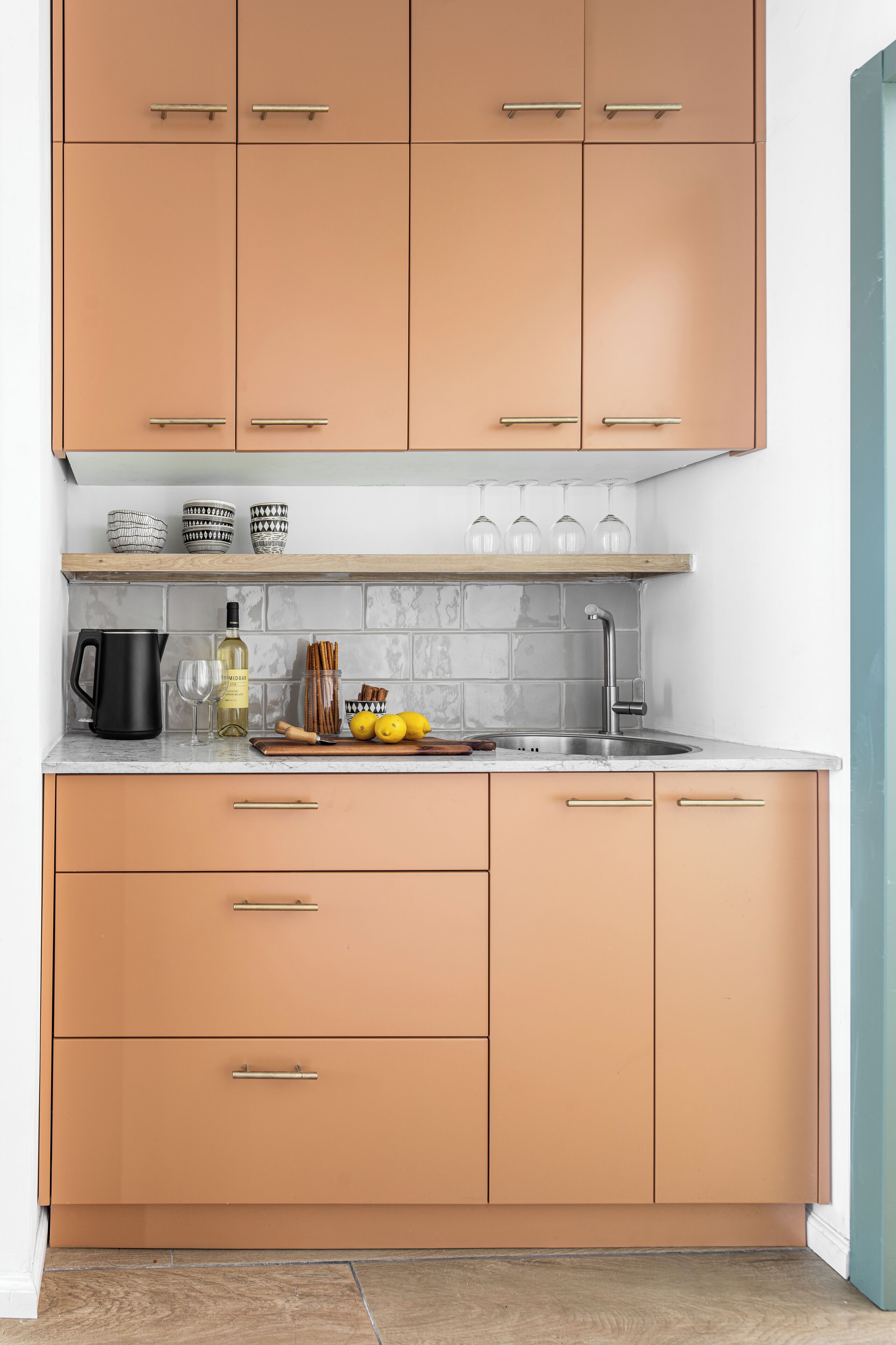 A kitchen with peach-colored cabinets, a marble countertop, a sink, and a wooden shelf above the countertop.