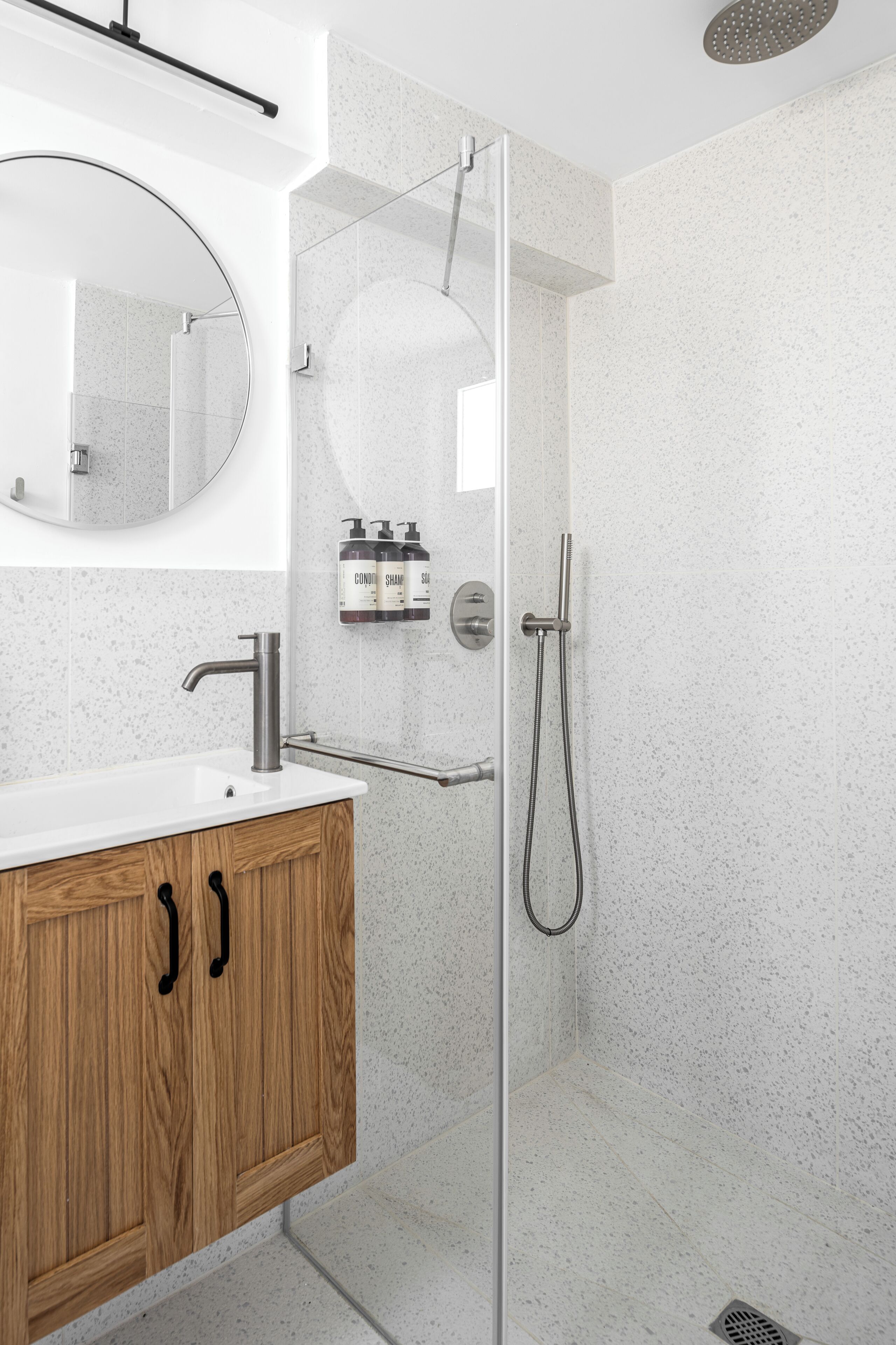 Un baño moderno con ducha de vidrio, tocador de madera con lavamanos y un espejo sobre el tocador.