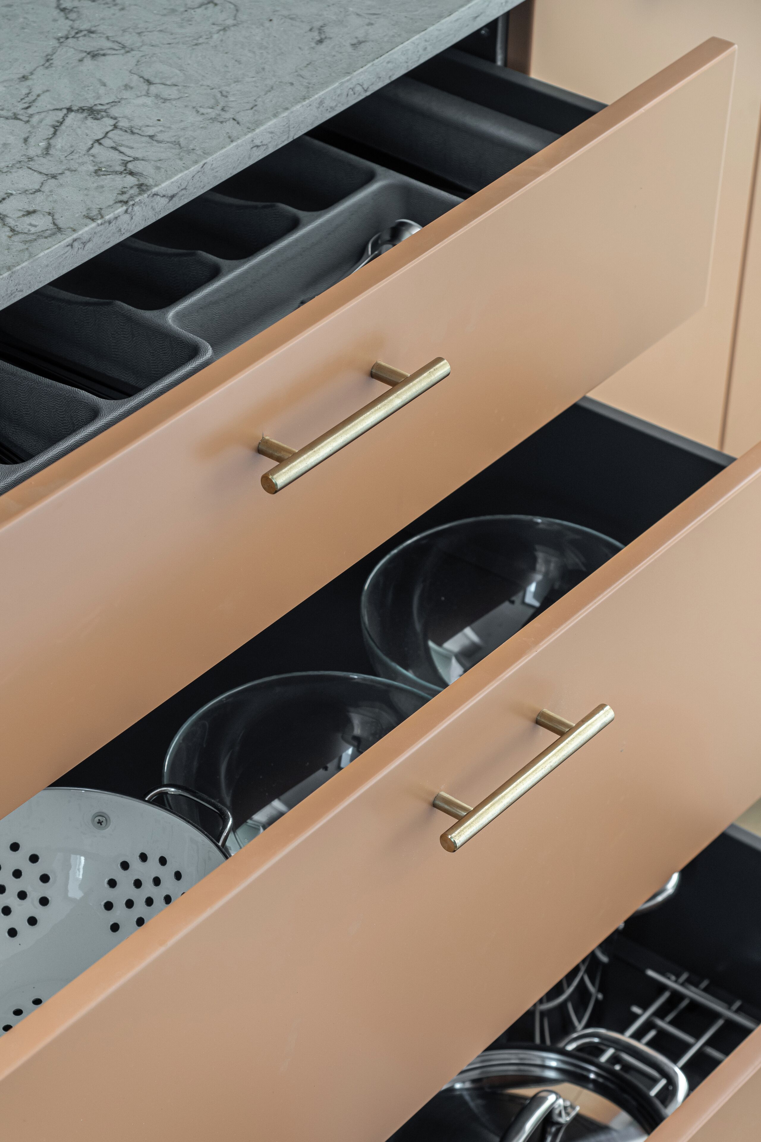 A kitchen drawer with two compartments, one containing a colander and the other holding a kettle.
