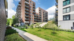 A modern apartment building with multiple balconies, a paved walkway, and a well-maintained lawn.