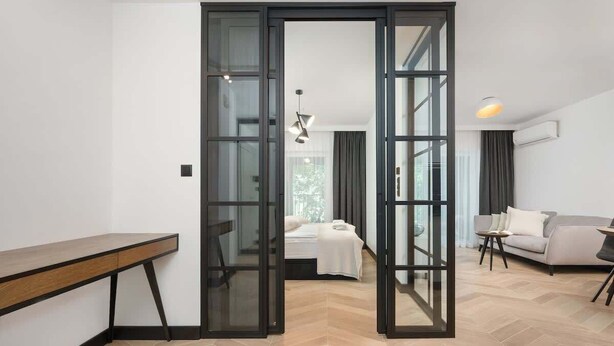 A modern interior with a wooden bench, a bed with a white duvet, a sofa, and a small table.