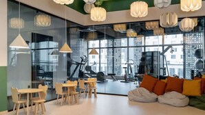 A modern gym with exercise equipment, large windows, and a seating area with a sofa and cushions.