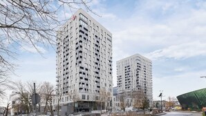 A modern high-rise building with multiple balconies and a parking lot in front.