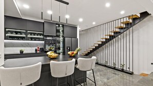 Una cocina moderna con una isla central, taburetes de bar y una escalera de peldaños de madera.