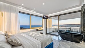 Un dormitorio moderno con una cama grande, una bañera y un balcón con vista al mar.